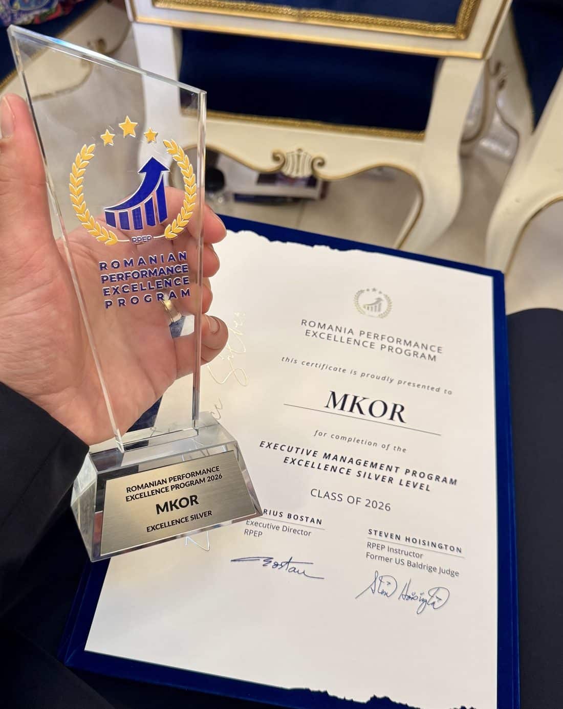 Trofeu de sticlă cu inscripția Romanian Performance Excellence Program 2026, MKOR, Excellence Silver, lângă certificatul Executive Management Program Excellence Silver Level, Class of 2026.